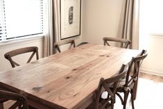 a wooden table with chairs around it in front of a window and framed pictures on the wall