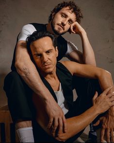 two men sitting on top of each other with their arms around one another's shoulders