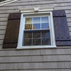 an open window on the side of a house with brown shutters and wood trim