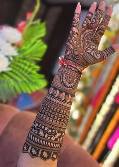 a woman's hand with henna tattoos on it and flowers in the background