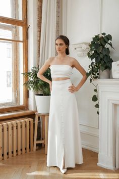 a woman standing in front of a window wearing a white dress with high slits