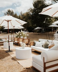 an outdoor seating area with white umbrellas and couches on the ground in front of trees