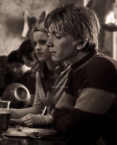 two people sitting at a table with plates and cups in front of them, one woman is looking off to the side