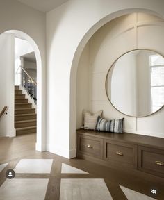 a hallway with a bench, mirror and stairs