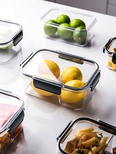 plastic containers filled with lemons, limes and other fruits on a white table