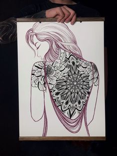 a person holding up a drawing in front of a black background with an intricate design on it