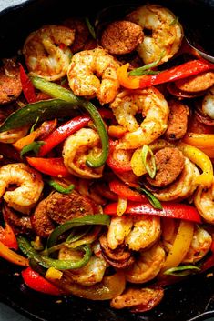 a skillet filled with shrimp, peppers, and sausage on top of a table