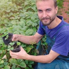 a man kneeling down in front of some potted plants and smiling at the camera