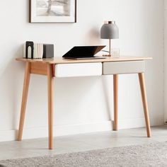 a desk with a laptop on it in front of a white wall and a gray rug