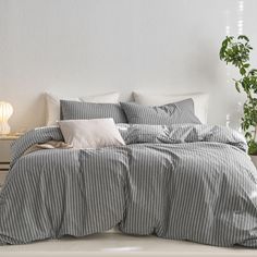 a bed with grey and white striped comforter next to a potted green plant