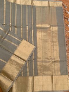 A very unique and stylish pure silk organza benarasi in a gorgeous gray shade with horizontal gold stripes. This is a very different benarasi, especially if you are looking to take a break from traditional sarees. The soft gold and gray look stunning together. The horizontal stripes give a modern look to the six yards. The fabric is extremely good quality silk organza. Saree is Silk Mark Certified. What is Kora Silk? Kora silk is untreated or un-dyed silk primarily made out of twisting only silk Gray Traditional Wear For Wedding And Festivals, Gray Chanderi Dupatta For Diwali, Gray Chanderi Traditional Wear For Festive Occasions, Traditional Gray Chanderi Dupatta, Elegant Gray Festive Traditional Wear, Elegant Gray Dupatta For Festive Occasion, Elegant Chanderi Dupatta With Kora Details, Elegant Dupatta With Kora In Traditional Drape, Elegant Chanderi Dupatta With Kora