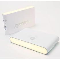 an electronic device is sitting next to a book on a white surface with light coming from it