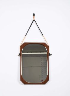 a mirror hanging from the side of a wall with a wooden frame and metal bar