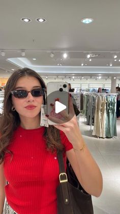 a woman taking a selfie with her cell phone in a clothing store while wearing sunglasses