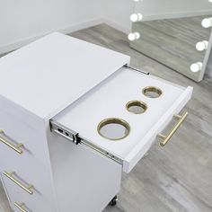 a white cabinet with three gold rings on it's drawers in front of a mirror