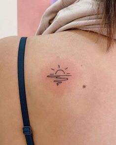 the back of a woman's shoulder with a sun tattoo on her left side