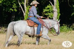 a woman riding on the back of a white horse in a field next to trees