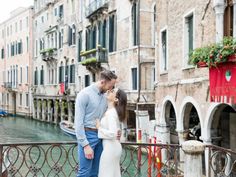 a man and woman standing next to each other in front of buildings on a canal