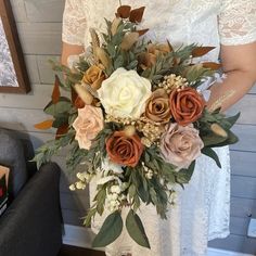 a woman in white dress holding a bouquet of flowers next to a wall with pictures on it