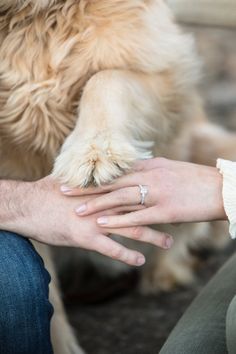 a person's hand with a wedding ring on their finger next to a dog