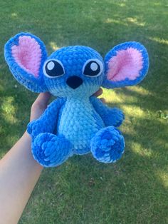 a hand holding a blue and pink crochet stitched stuffed animal in the grass