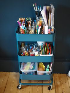 a blue cart filled with office supplies on top of a wooden floor