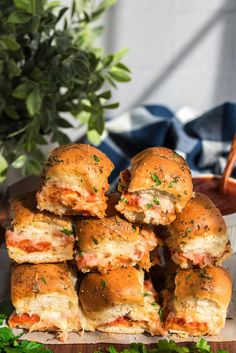 a pile of sliders sitting on top of a wooden cutting board next to a potted plant