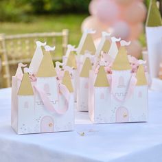 small princess castle bags on a table with pink flowers in the center and balloons behind them