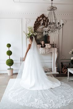 a woman in a white wedding dress is standing near a chandelier and fireplace