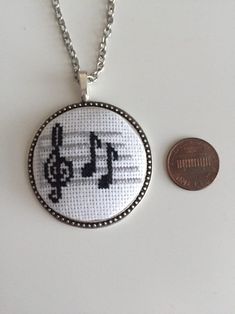 a cross stitch necklace next to a penny