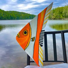 an orange and white fish kite sitting on top of a metal fence next to a body of water