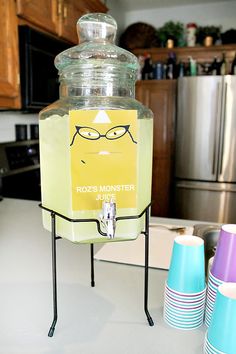 a beverage dispenser sitting on top of a kitchen counter next to cups