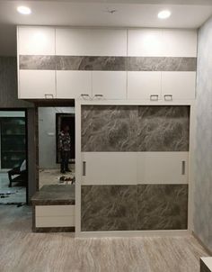 a room with white cabinets and grey marble wall covering it's walls, while someone is standing in the doorway