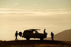 three people standing on top of a hill next to a van