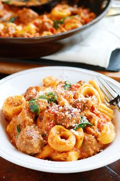 a white plate topped with pasta covered in sauce and meatballs next to a fork