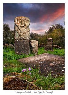 a stone statue sitting in the middle of a lush green field under a cloudy sky