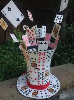 a hat made out of playing cards on top of a cement slab with trees in the background