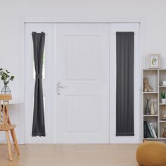 a living room with white walls and black drapes on the door, next to a wooden chair