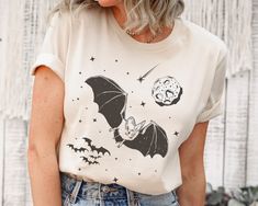 This hand drawn retro bat UNISEX shirt makes a great halloween gift for goblincore lovers. The  shirts have a soft and light feel and are comfortable and flattering for everybody. ---------------------------------------------------------- SIZING: See sizing charts * Not sure about the sizing? Lay your favorite shirt flat and measure from armpit to armpit (width) and top to bottom (length). * Women may want to order one size smaller for slimmer fit (UNISEX apparel). * Please order size carefully Halloween Goblincore T-shirt With Graphic Print, Goblincore Halloween Short Sleeve T-shirt, Goblincore Halloween T-shirt With Short Sleeves, Halloween Goblincore Graphic T-shirt, Bat Shirt, Vampire Bat, Halloween Bat, Pumpkin Season, Affinity Designer