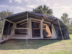 a tent set up in the middle of a field with trees and grass around it