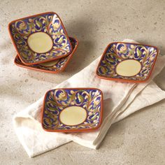 two square dishes sitting on top of a white napkin next to each other in front of a bowl