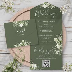 the wedding stationery is set on top of a wooden platter with greenery and white flowers