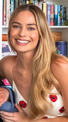 a woman holding a baby in her arms and smiling at the camera with bookshelves behind her