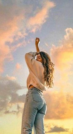 a woman standing on top of a hill with her arms in the air and looking up