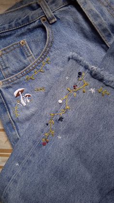 an old pair of blue jeans with embroidered flowers and stars on them sitting on a wooden surface