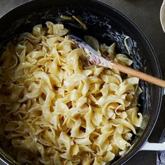 a pot filled with pasta and sauce on top of a counter next to a wooden spoon