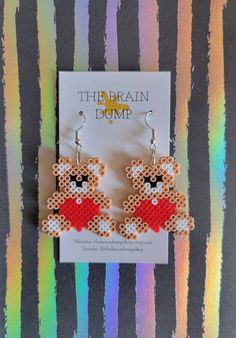 a pair of earrings with a teddy bear on the front and bottom, sitting in front of a rainbow striped background