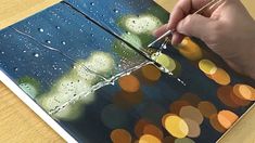 a person is painting on a piece of paper with water and lights in the background