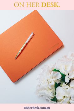 an orange notebook with a pen on it and white flowers next to it that says, what is the best way to write on her desk?