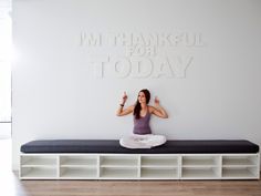 a woman sitting on top of a bench in front of a wall with words above her